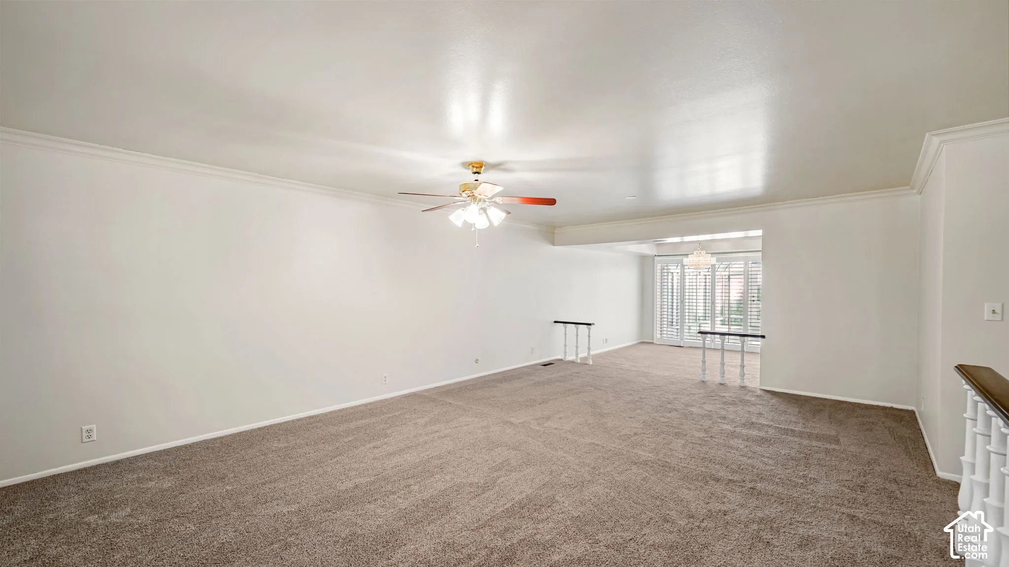 Spacious room featuring neutral carpeting, crown molding, and a ceiling fan with integrated lighting