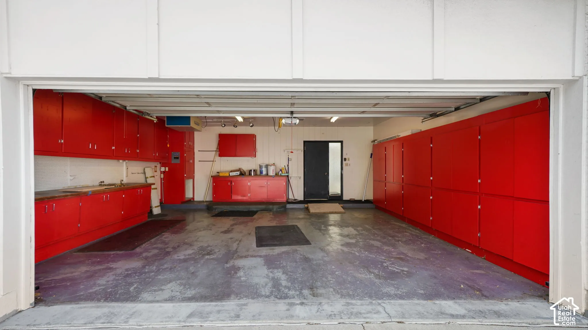 Spacious garage featuring extensive red cabinetry for storage, a utility sink, a workbench area, and concrete flooring