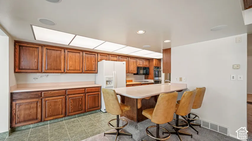 Kitchen area featuring a built-in breakfast bar, wood cabinetry, tile flooring, and recessed ceiling lighting