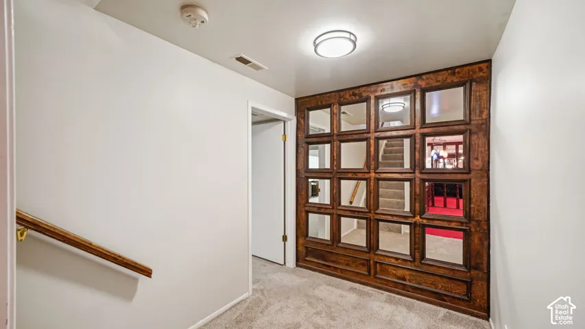 Wood-paneled accent wall with mirrored insets, overhead flush mount lighting, light carpeting, and a wood handrail