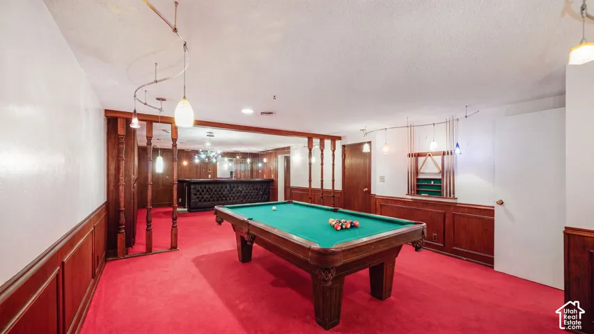 AI Recreation space featuring red carpeting, dark wood wainscoting, and a built-in bar with dark wood paneling