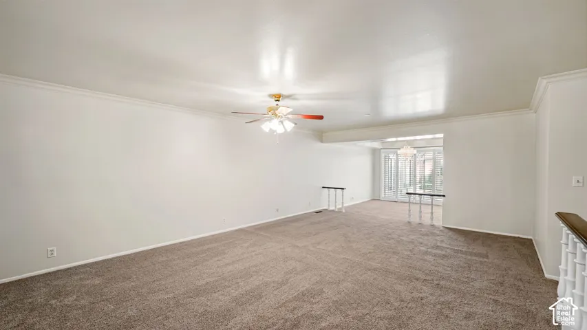 Spacious room featuring neutral carpeting, crown molding, and a ceiling fan with integrated lighting