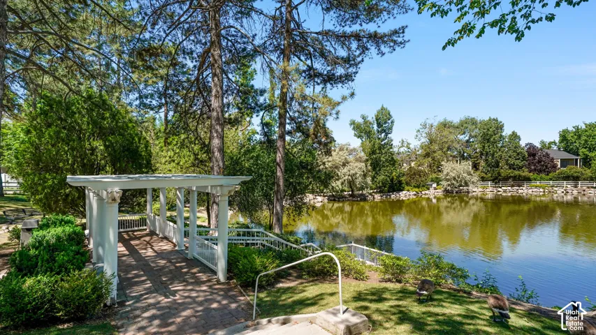 Waterfront property with a white pergola, surrounded by mature trees and established landscaping