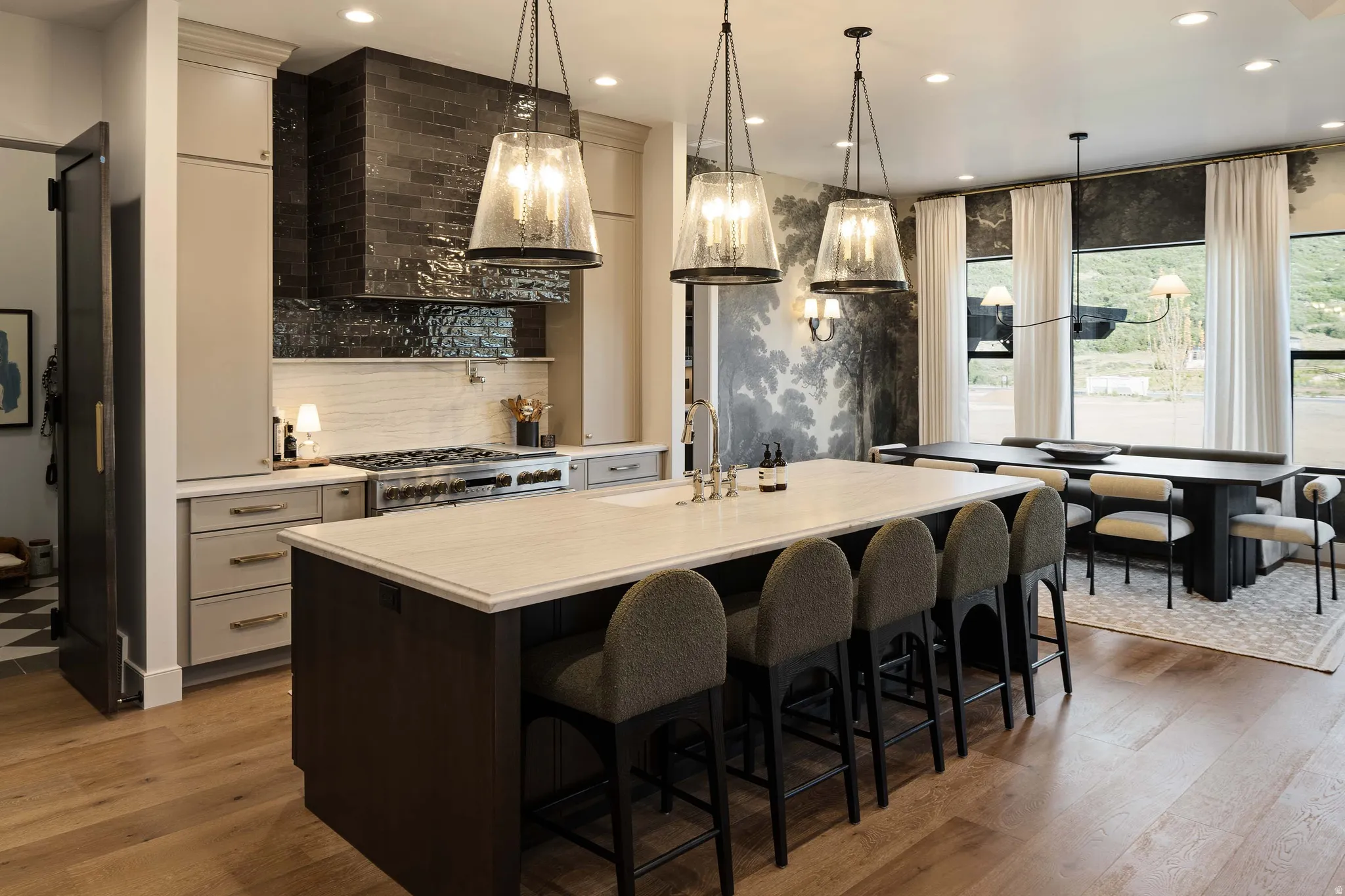 Gourmet kitchen featuring a large island with seating, a professional-grade range, custom cabinetry, wood-finish flooring, and a dining area with expansive windows