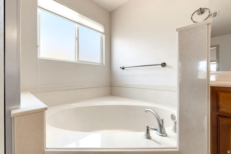 Corner soaking tub with brushed nickel fixtures, surrounded by a light-toned tile deck