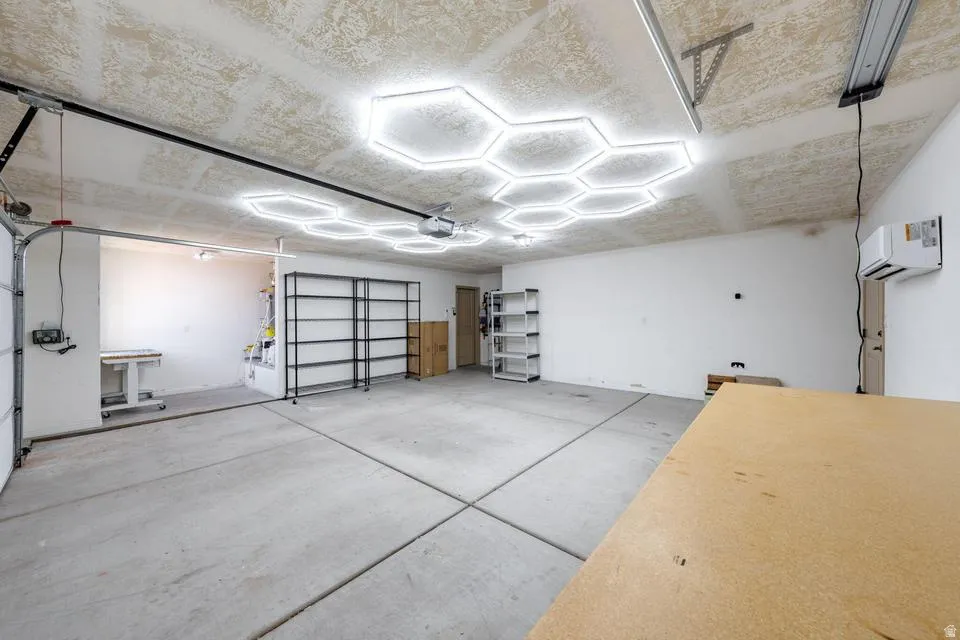 Spacious garage featuring a concrete floor, bright hexagonal ceiling lighting, white painted walls, and an overhead garage door