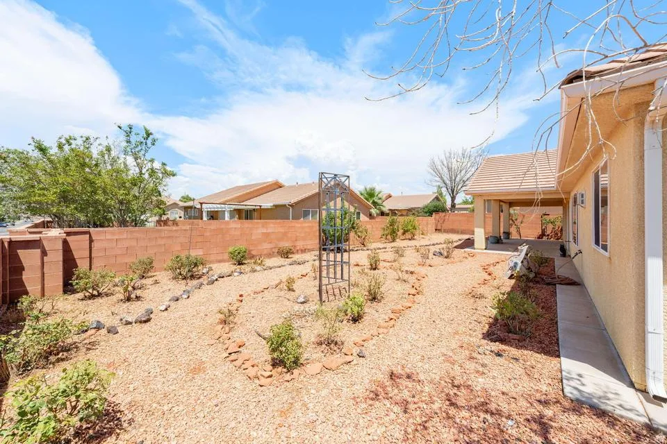 Expansive backyard featuring a red block wall perimeter, gravel ground cover, a metal garden trellis, and a covered patio area