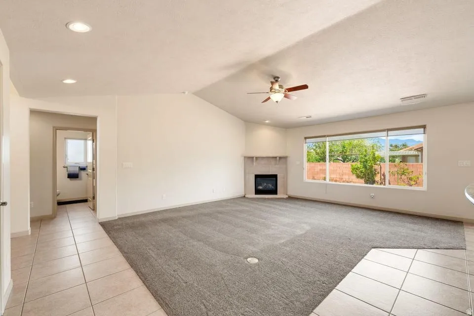 Spacious living area featuring a corner fireplace with a mantel, a ceiling fan, and large windows
