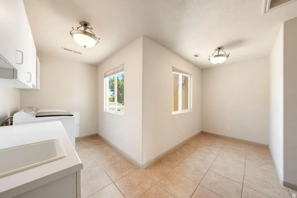 Utility room featuring tile flooring, white cabinetry, a built-in sink, and two windows