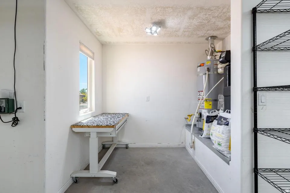 Utility room featuring a window, overhead lighting, a built-in shelf, and concrete flooring