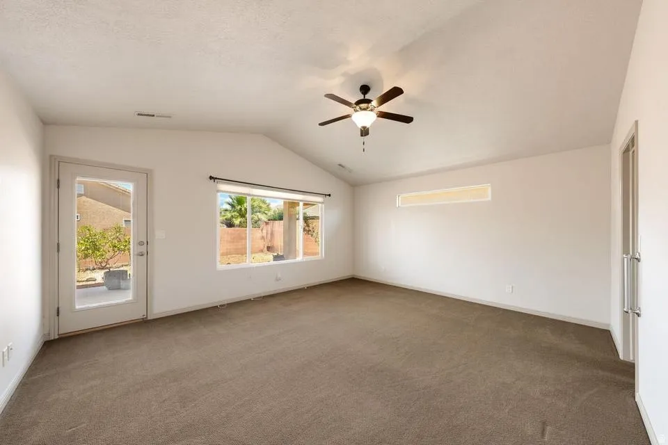 Spacious room featuring vaulted ceilings, a ceiling fan with integrated lighting, and neutral-toned carpeting