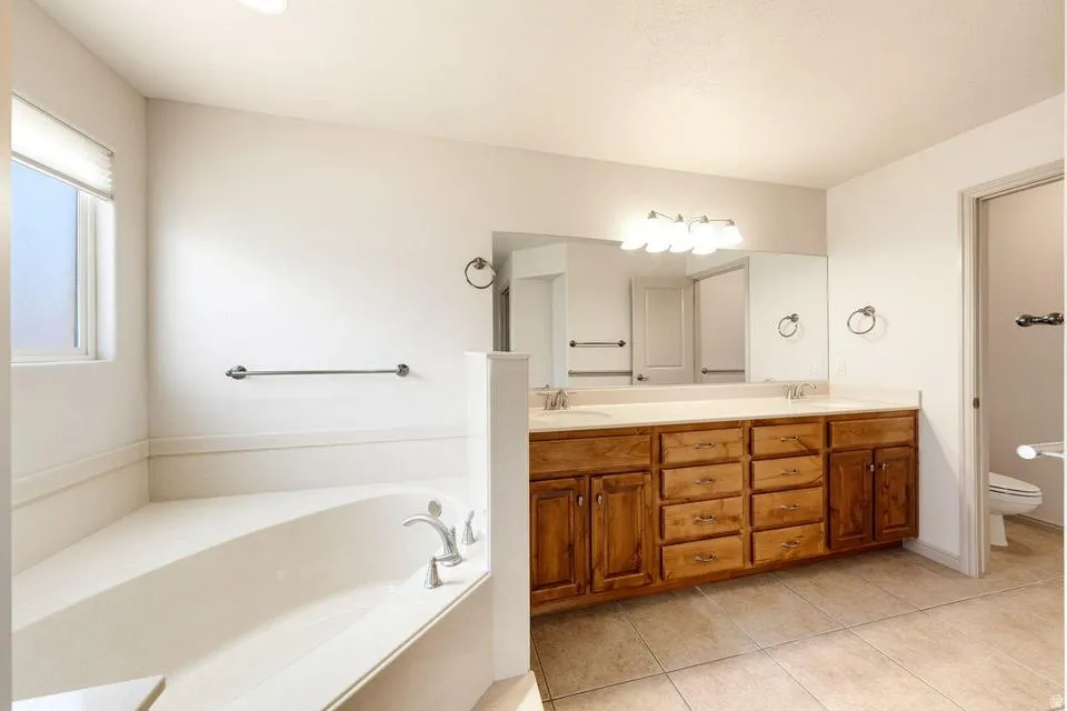 Full bathroom featuring a corner soaking tub, a double vanity with wood cabinetry, a large wall mirror, and tile flooring