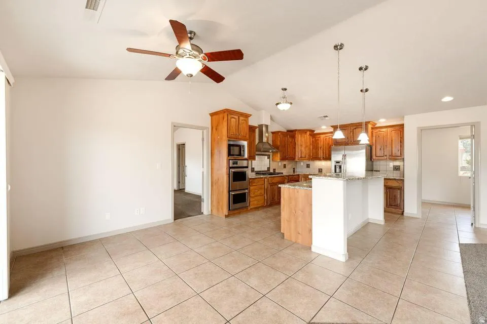 Open-concept kitchen featuring wood cabinetry, stainless steel appliances, a kitchen island with pendant lighting, and tile flooring