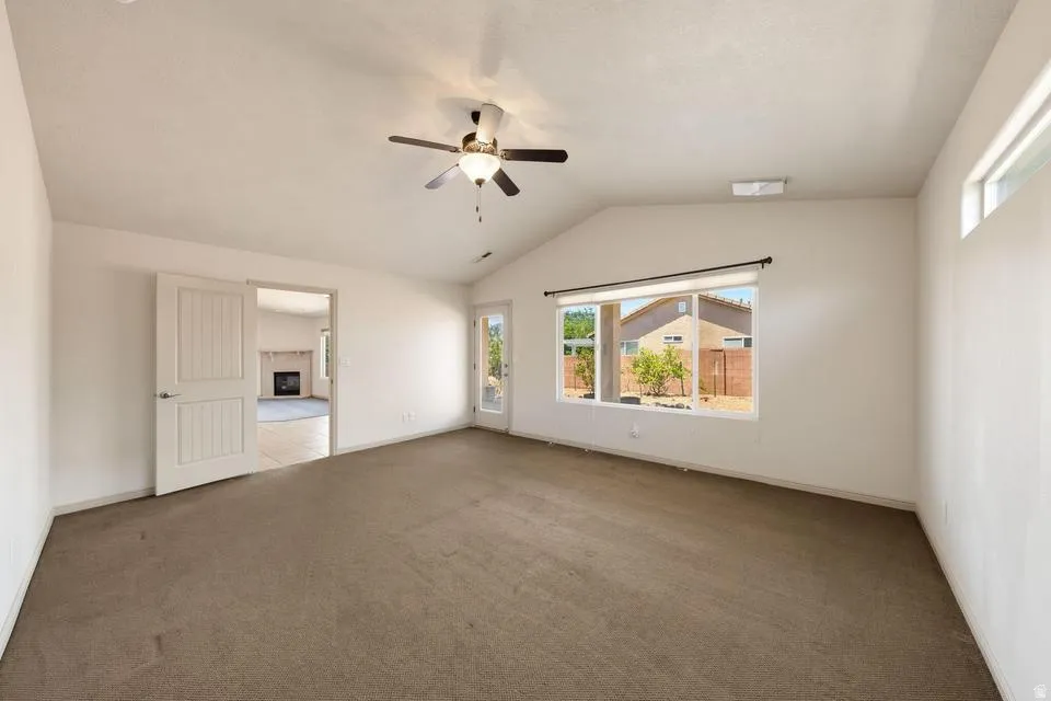 Spacious room featuring vaulted ceilings, a ceiling fan, broad window, and carpeted flooring