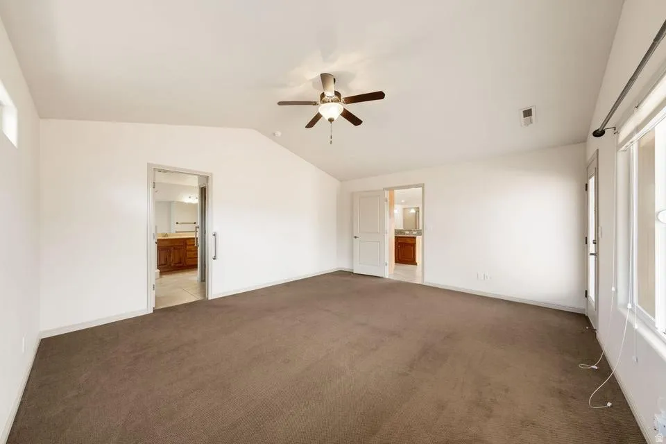 Spacious room featuring vaulted ceilings, neutral-toned carpet flooring, and a ceiling fan with integrated lighting