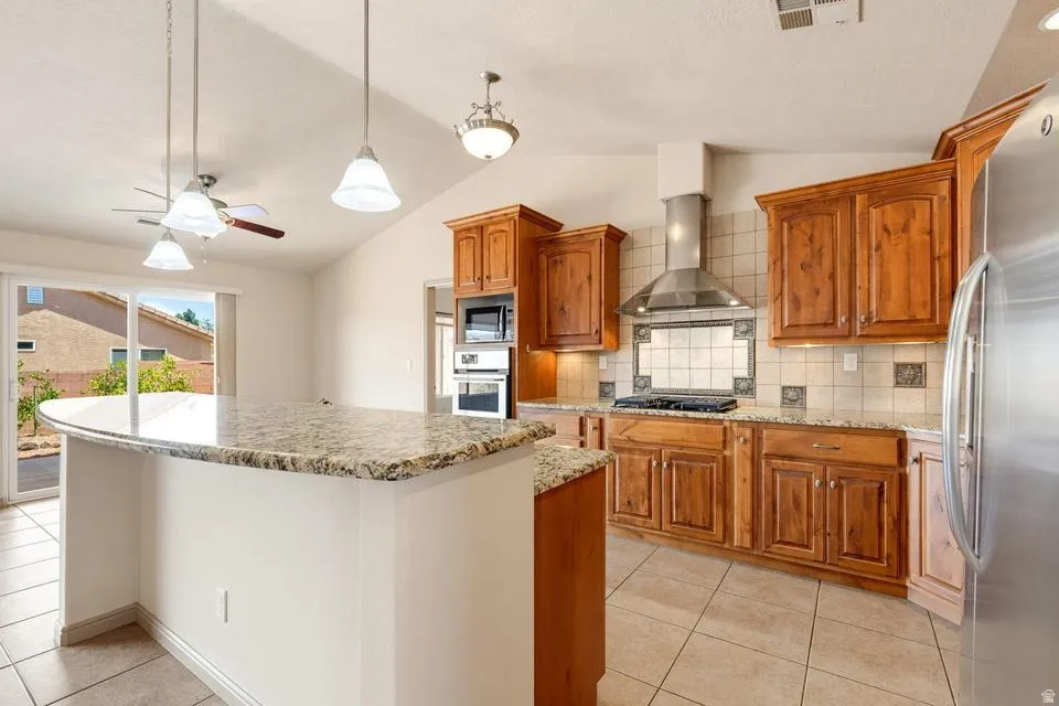 Kitchen featuring a curved granite-finish island, vaulted ceilings, wood-finish cabinetry, stainless steel appliances, and tile flooring