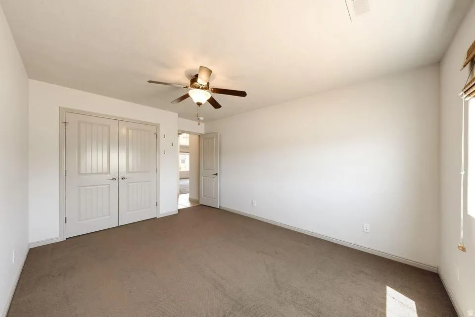 Spacious room featuring neutral carpeting, a ceiling fan with integrated lighting, and a window with blinds