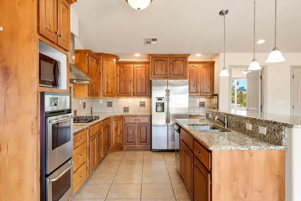 Spacious kitchen featuring extensive wood cabinetry, stainless steel appliances including a built-in oven and microwave, granite countertops, and a large island with a breakfast bar