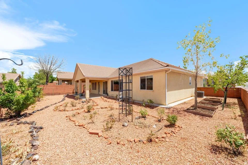 Expansive rear yard featuring gravel landscaping, mature trees, a covered patio, and raised garden beds