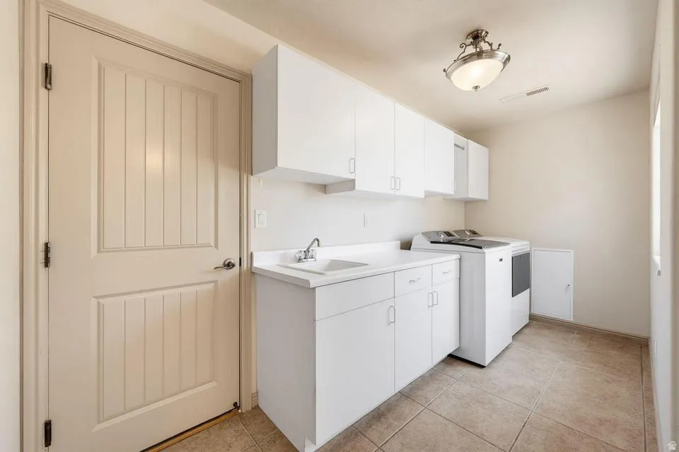 Dedicated utility space featuring extensive white cabinetry, a built-in sink with a countertop, tiled flooring, and a paneled interior door