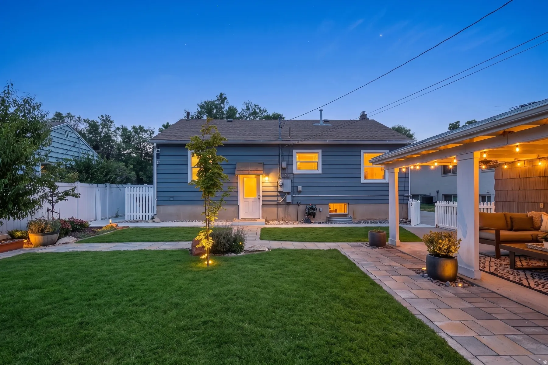 Manicured backyard featuring a covered patio with string lighting, paver pathways, a privacy fence, and mature landscaping