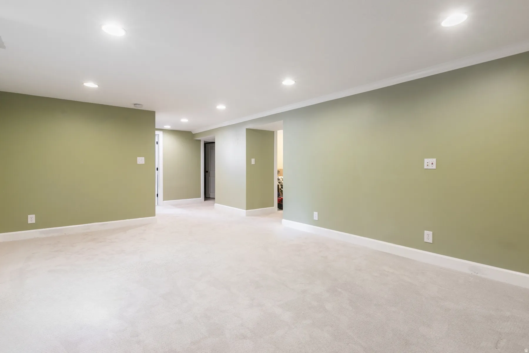 Spacious room featuring light olive walls, white trim, recessed lighting, and light-colored carpeting