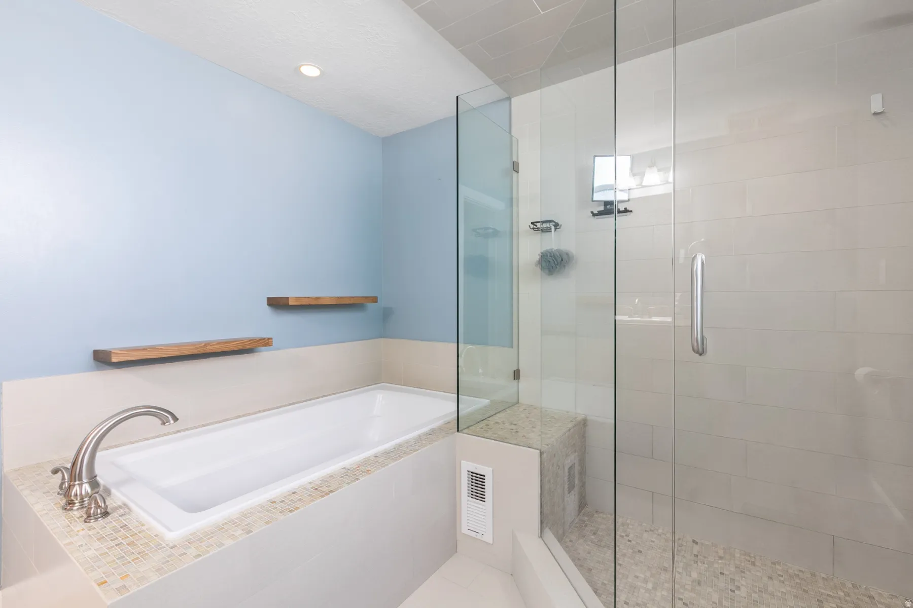 Contemporary bathroom featuring a built-in tub with brushed nickel fixtures, glass-enclosed shower with a bench, light-toned wall tile, and pebble-finish shower floor