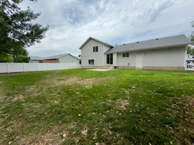 Spacious backyard featuring a substantial lawn area, full vinyl fencing, and a concrete patio