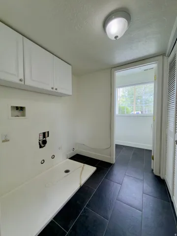 Laundry area with dark tile flooring, white shaker-style cabinetry