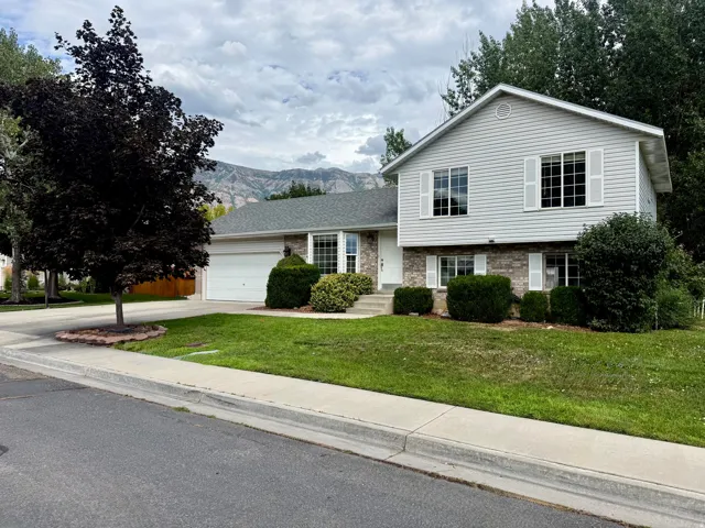 Tri-level home featuring light gray siding with brick accents, an attached garage, and a lush green lawn