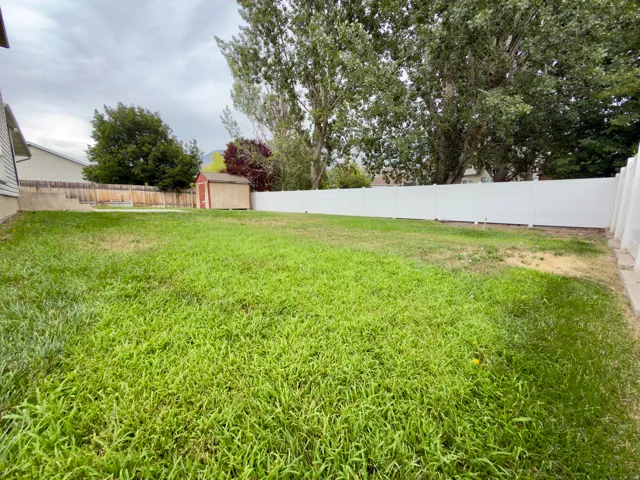 Expansive backyard featuring a white vinyl fence, an additional wood fence, mature trees, and a storage shed