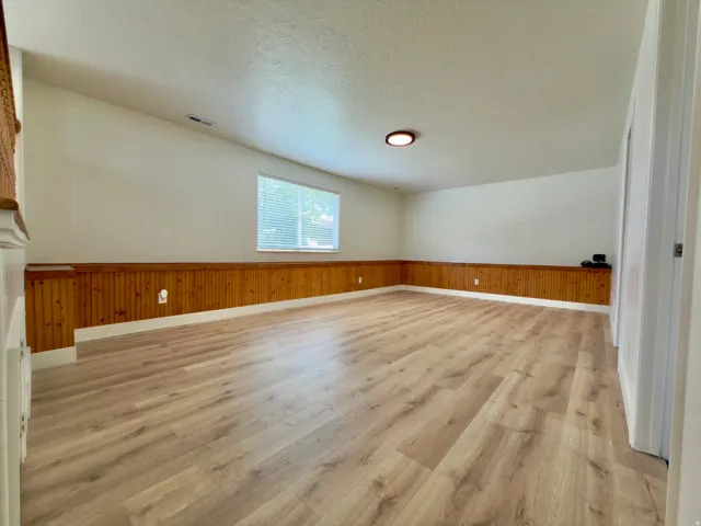 Spacious family room featuring LVP flooring, wood paneling, and a single window with blinds