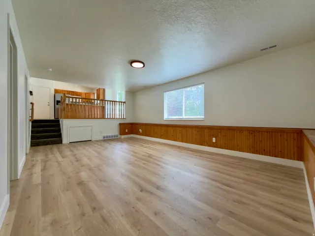 Large family room featuring LVP flooring, a large window with blinds, and paneled wainscoting