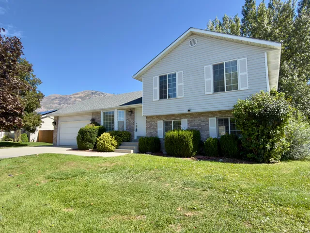 Split-level exterior with light gray siding, brick veneer accent, white window shutters, and a two-car garage