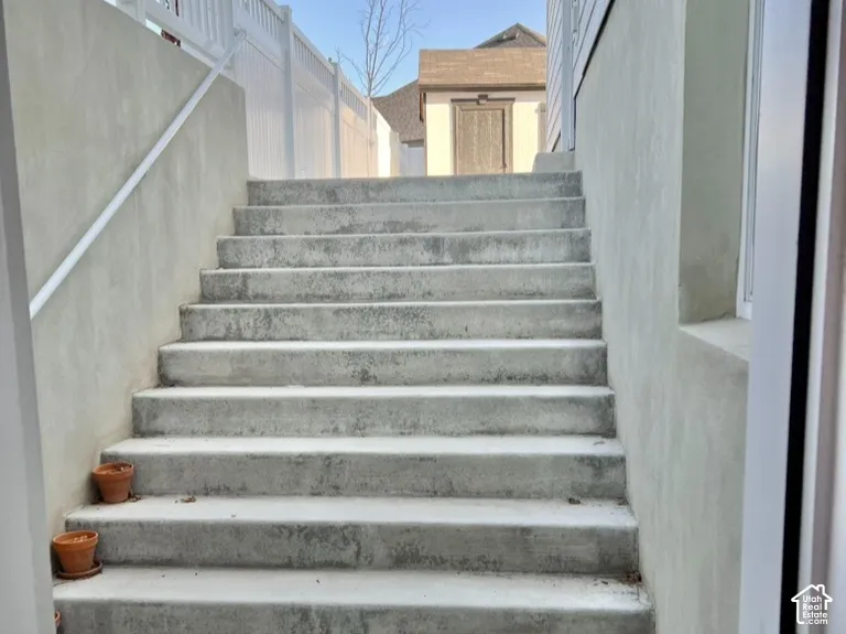 Exterior concrete staircase with an adjacent white vinyl fence and a small detached shed