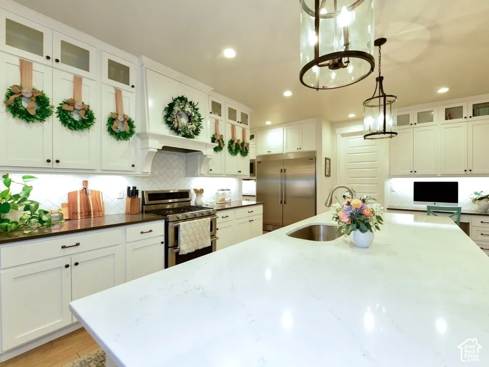 Kitchen featuring a large central island with an undermount sink, white shaker cabinetry, stainless steel appliances, dark countertops, and a white herringbone tile backsplash