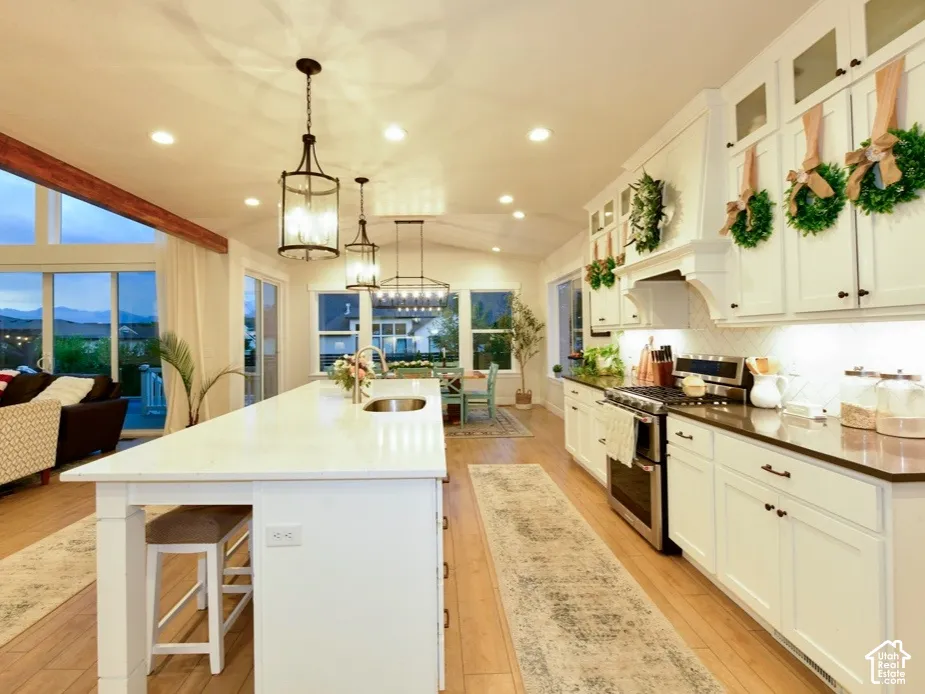 Open-concept kitchen and living area featuring white cabinetry, wood-finish flooring, a large kitchen island with integrated sink, stainless steel appliances, and a tiled backsplash