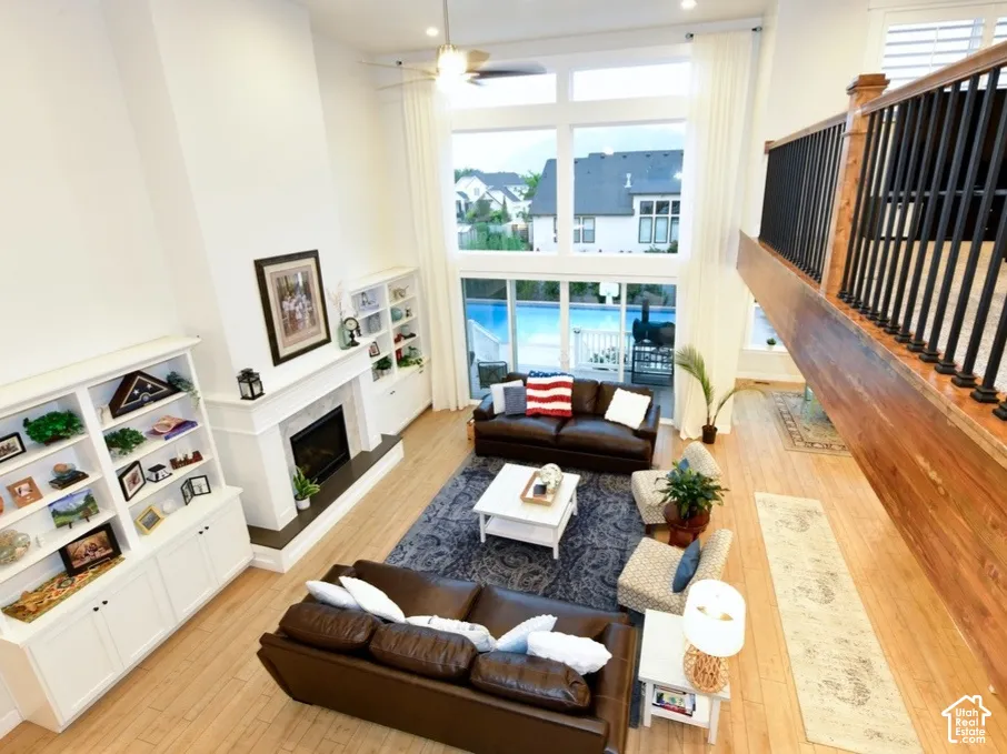 Two-story living room featuring a fireplace with white mantel, built-in shelving, wood-finish flooring, and a large window wall overlooking an outdoor pool