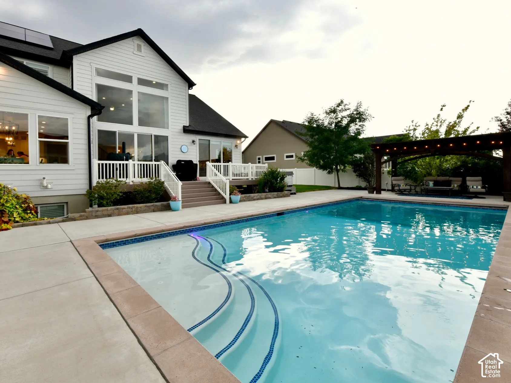 Spacious backyard featuring an in-ground swimming pool with integrated steps, extensive concrete decking, and a wood pergola
