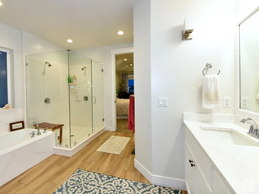 Spacious bathroom featuring a dual walk-in glass shower, built-in soaking tub, single vanity with integrated sink, and wood-finish flooring