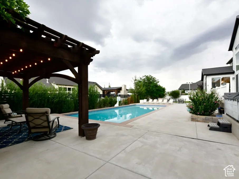 Expansive concrete patio featuring a rectangular swimming pool, a freestanding hot tub, and an attached pergola with string lighting