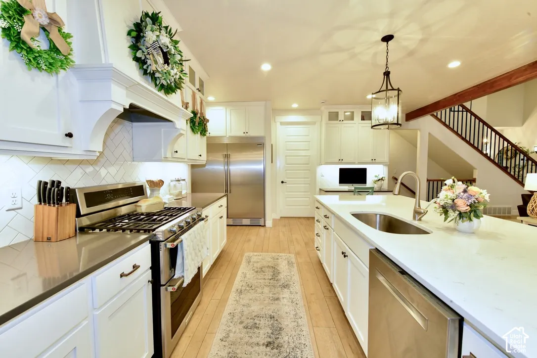 Spacious kitchen featuring white cabinetry, stainless steel appliances, light wood-finish flooring, a herringbone tile backsplash, and an island with an undermount sink