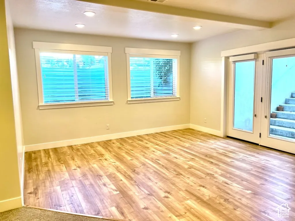 Spacious room featuring wood-finish flooring, two windows with blinds, recessed lighting, and a double glass-paneled door