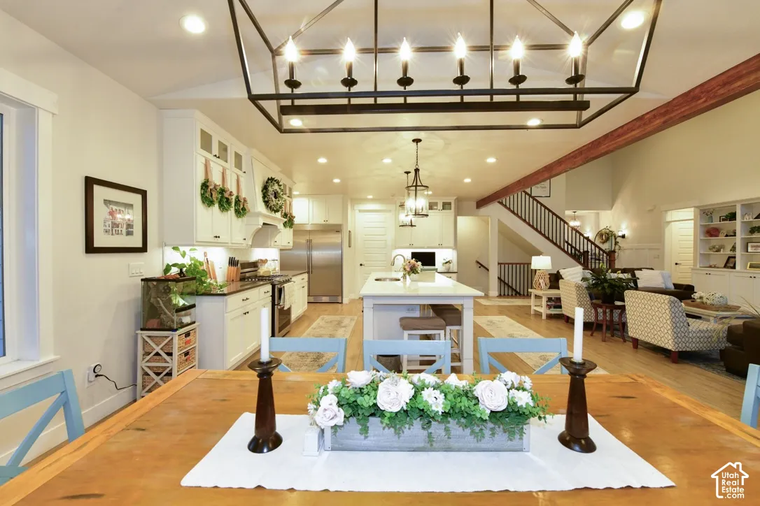Open-concept living area featuring a kitchen with white cabinetry and stainless steel appliances, a central island with seating, a dining area with a wood table, and a living room with built-in shelving