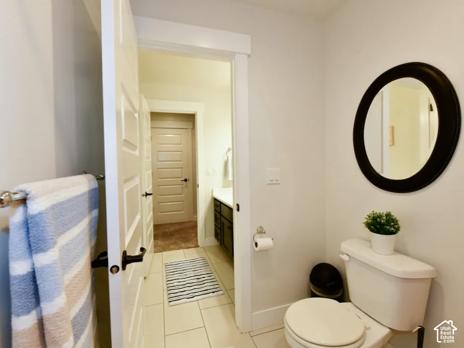 Bathroom featuring a white toilet, a circular mirror with a dark frame, and light-colored tile flooring