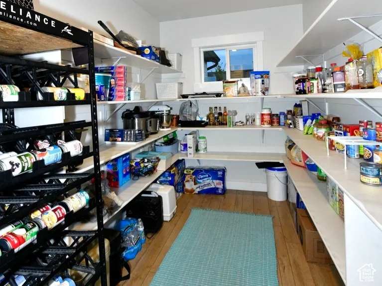 Spacious pantry featuring extensive white shelving, wood-finish flooring, recessed lighting, and a window for natural light