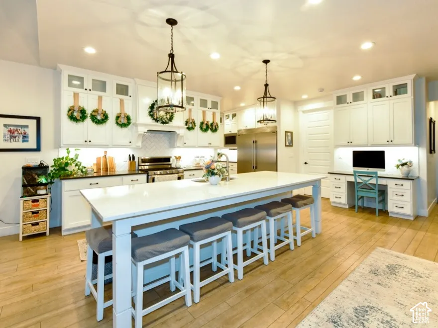 Spacious kitchen featuring an oversized island with seating, white shaker cabinetry, stainless steel appliances, and wood-finish flooring