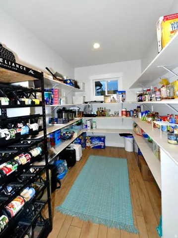 Spacious pantry featuring extensive white shelving, wood-finish flooring, recessed lighting, and a window for natural light