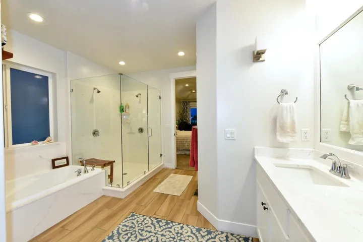 Spacious bathroom featuring a dual walk-in glass shower, built-in soaking tub, single vanity with integrated sink, and wood-finish flooring