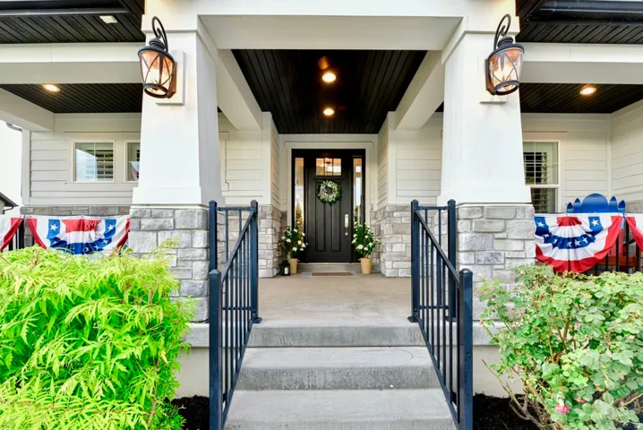 Inviting covered porch with stone base pillars and exterior wall sconces